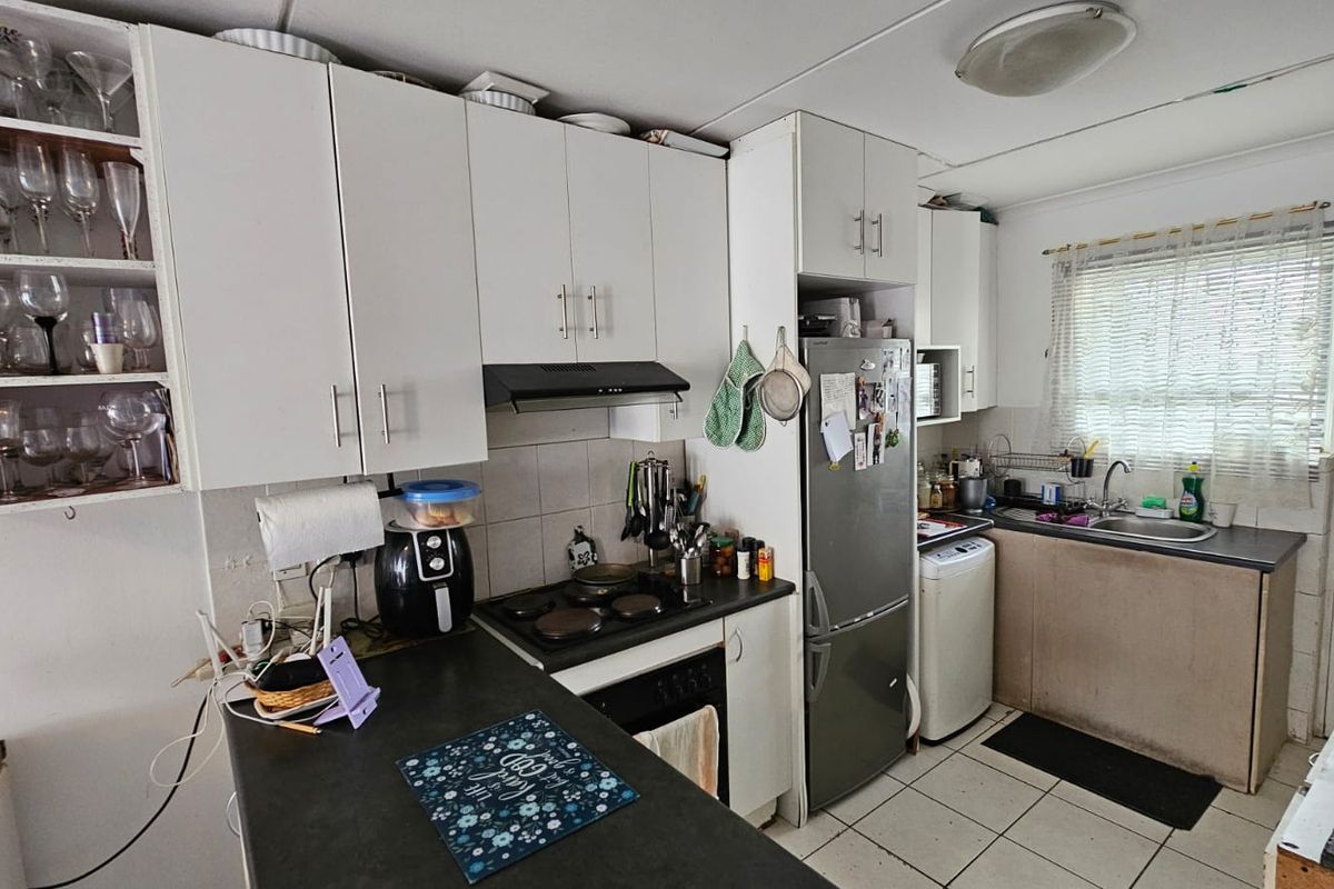 Functional kitchen featuring white cabinetry, dark laminate countertops, integrated hob and oven, and tiled flooring, offering a practical layout for daily use.