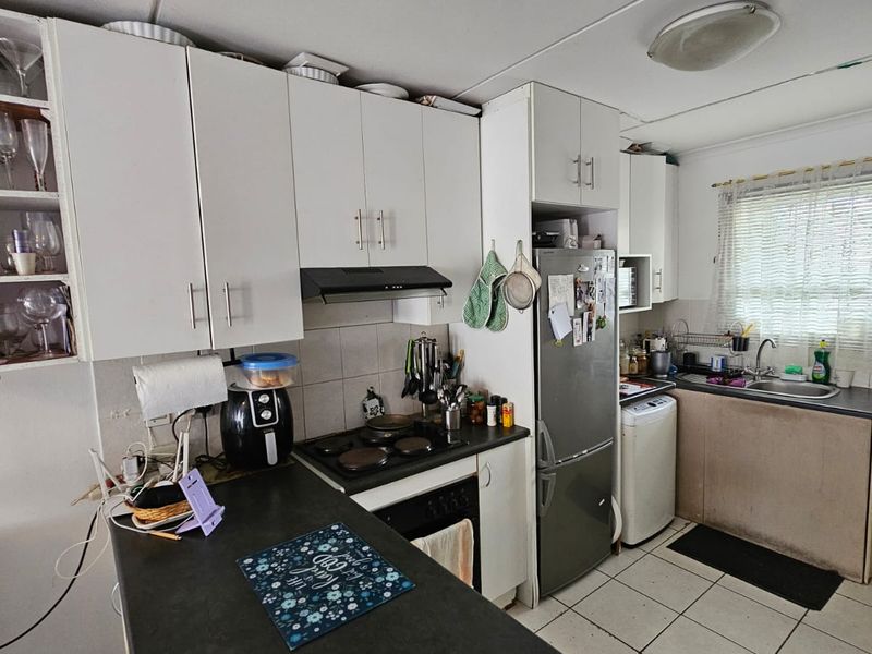 Functional kitchen featuring white cabinetry, dark laminate countertops, integrated hob and oven, and tiled flooring, offering a practical layout for daily use.