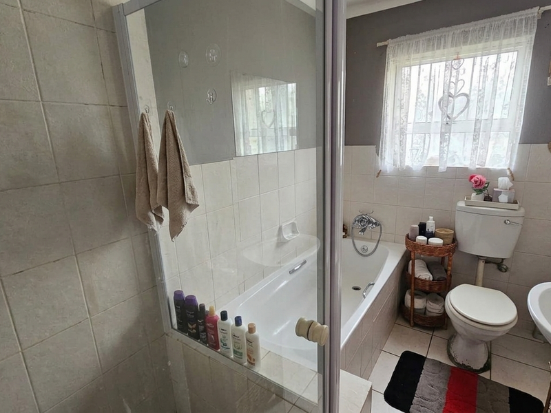 A functional bathroom featuring a bathtub, separate shower enclosure, pedestal basin, and toilet with neutral wall tiling.
