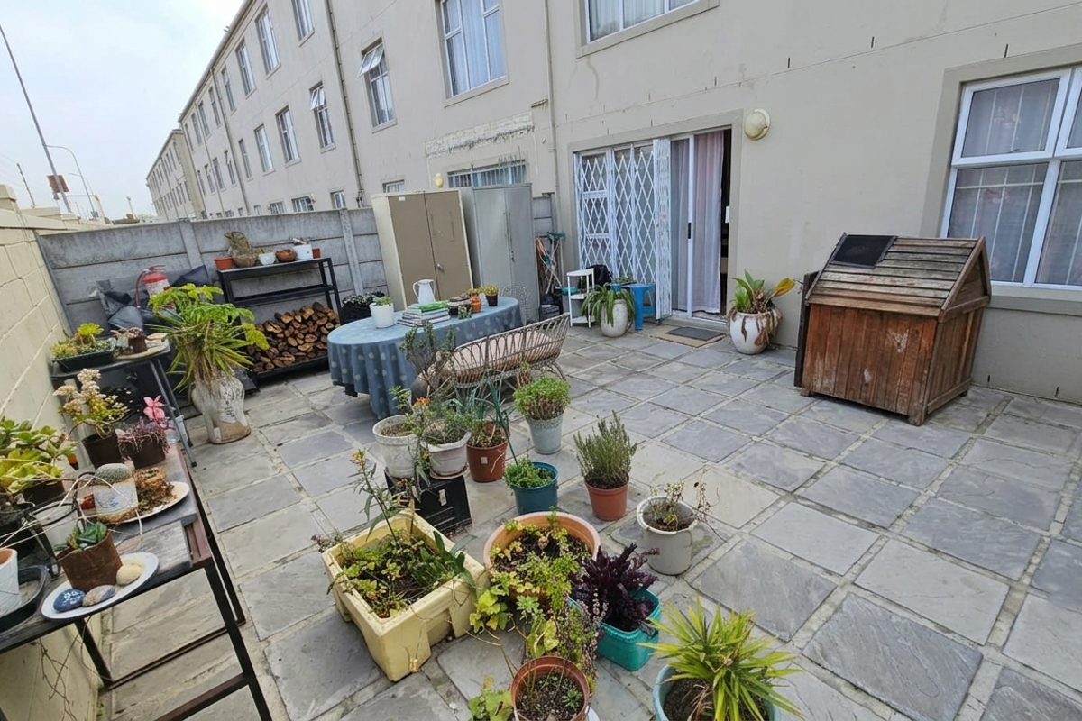 A paved rear courtyard area featuring a sliding door entrance with security gate and precast concrete boundary walls.