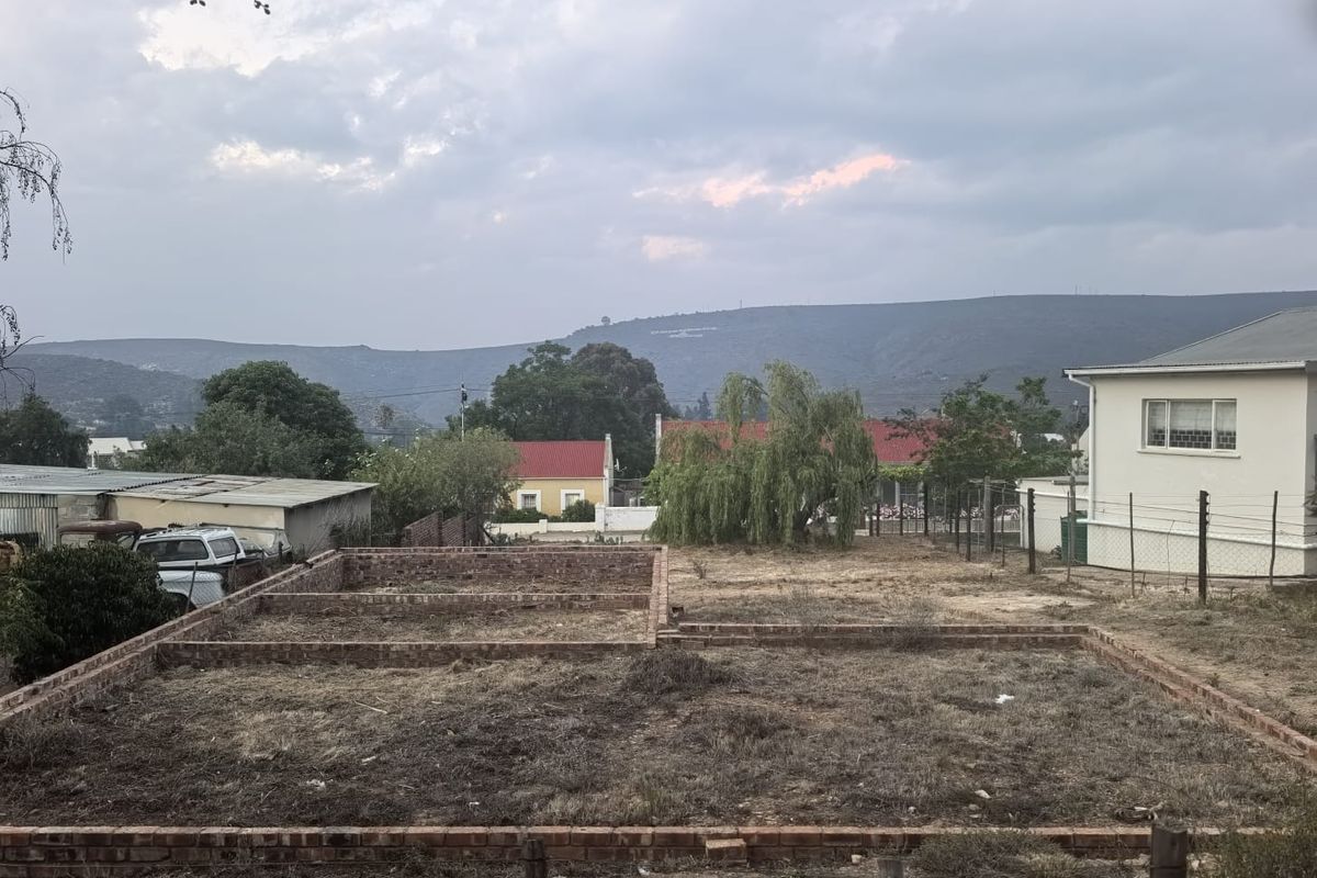A vacant residential plot featuring a brick foundation layout, surrounded by established neighborhood properties and scenic mountain views.