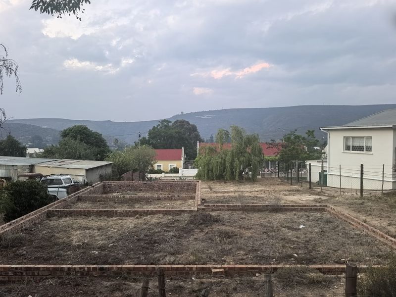 A vacant residential plot featuring a brick foundation layout, surrounded by established neighborhood properties and scenic mountain views.