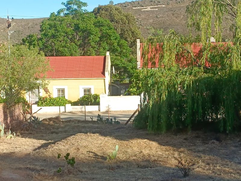 View of the property frontage featuring traditional buildings with red corrugated metal roofs, set against a natural hillside backdrop.