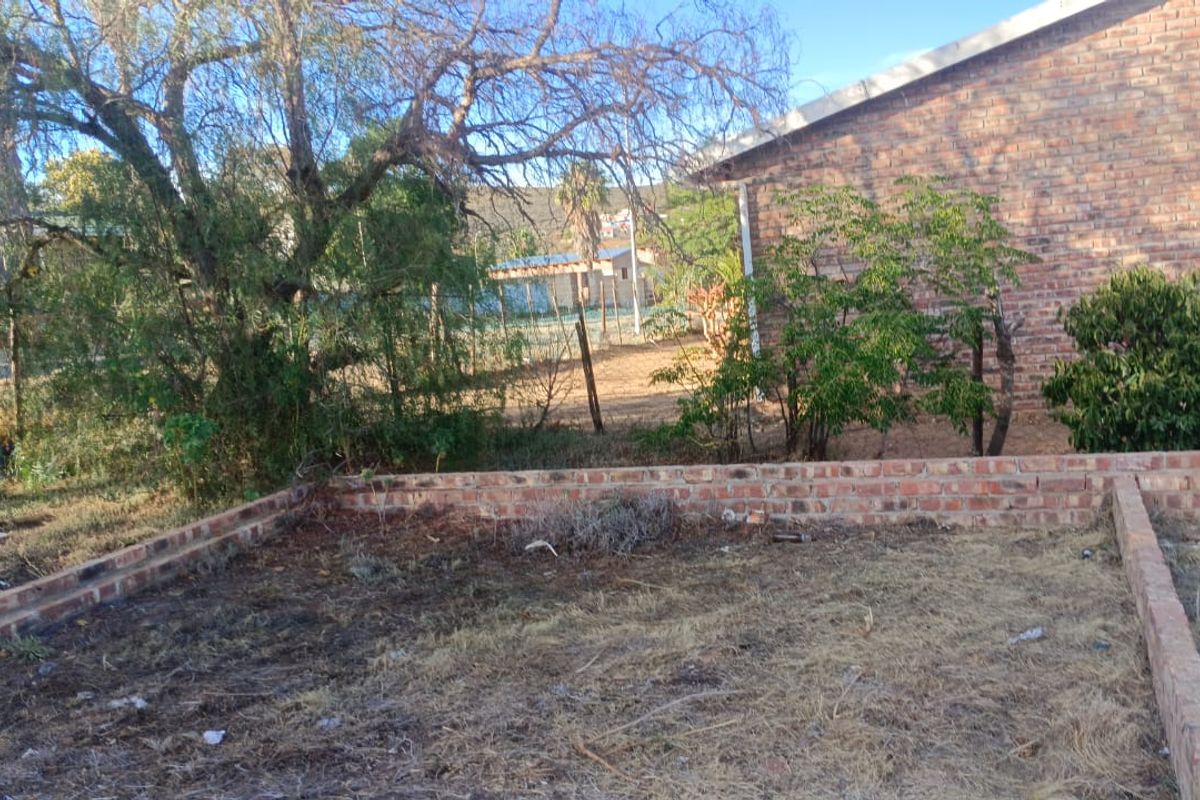A view of the rear yard featuring a low brick retaining wall, face brick building exterior, and established trees on the residential plot.
