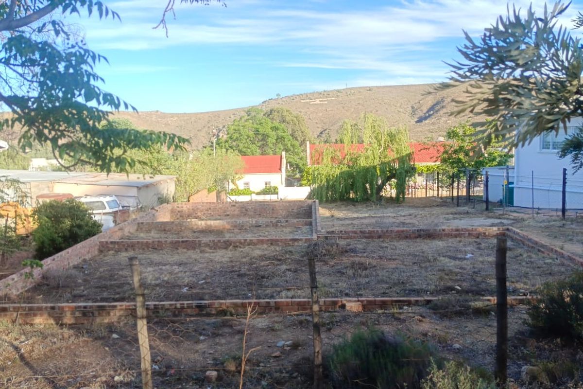 A vacant residential plot featuring a brick foundation outline, set against a scenic mountain backdrop in a quiet neighborhood.