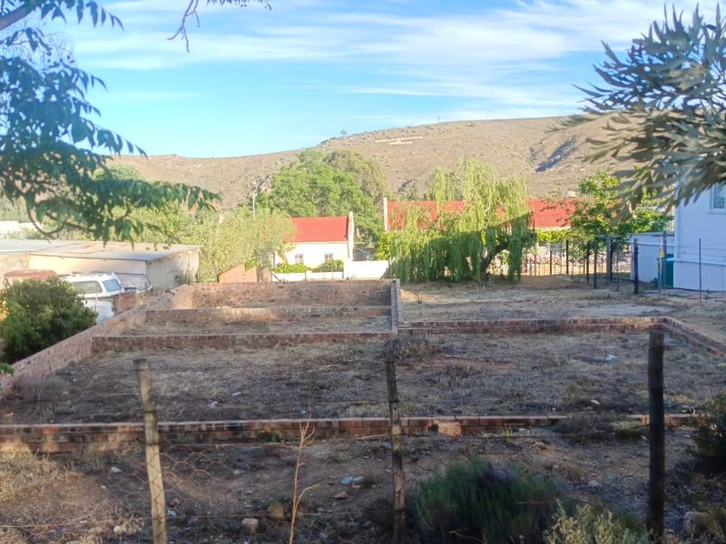 A vacant residential plot featuring a brick foundation outline, set against a scenic mountain backdrop in a quiet neighborhood.
