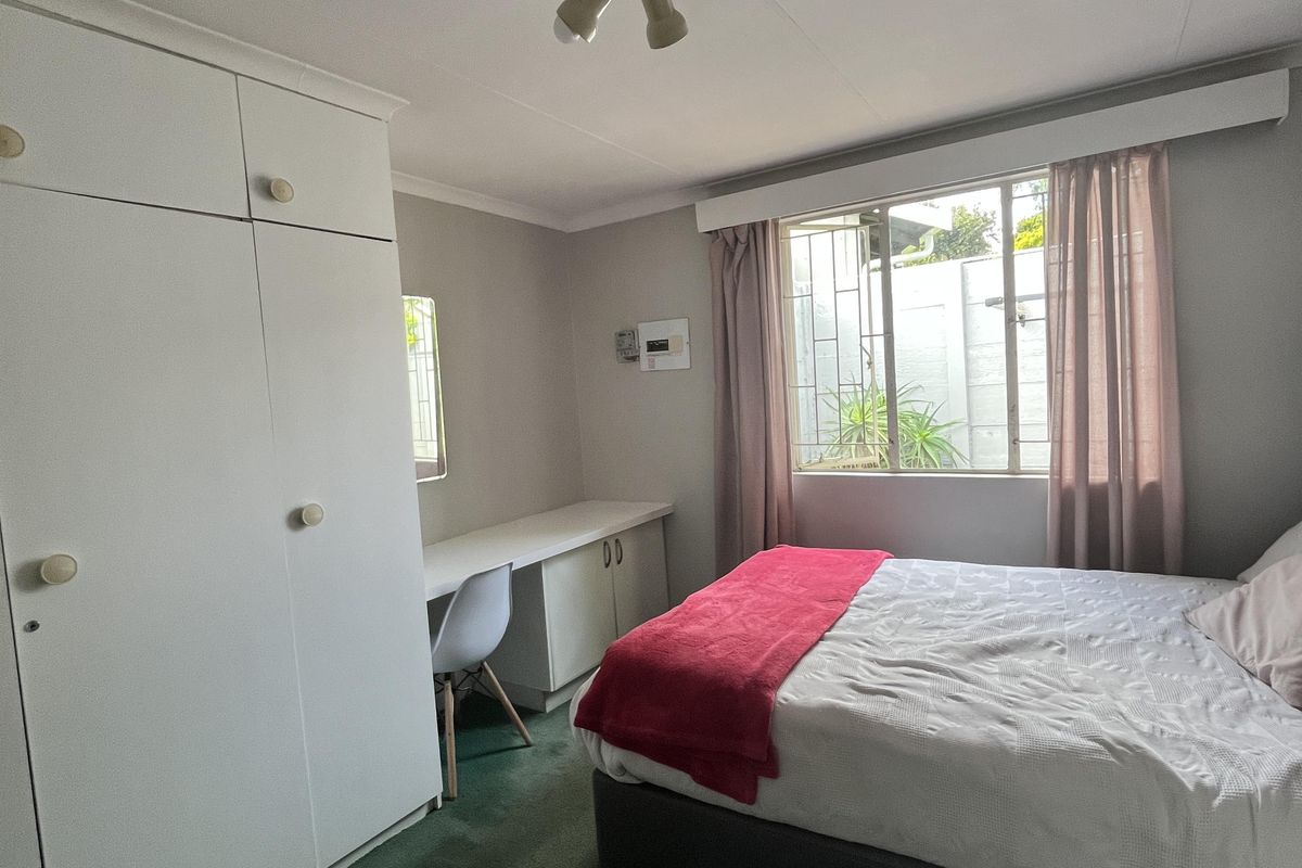 A bedroom featuring built-in cupboards, a built-in desk, and security bars on the window. The room has carpeted flooring and neutral wall finishes.
