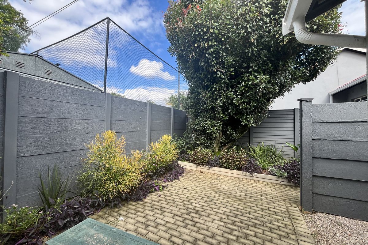 A private rear courtyard featuring paved flooring, established garden beds, and secure boundary walling with perimeter fencing.