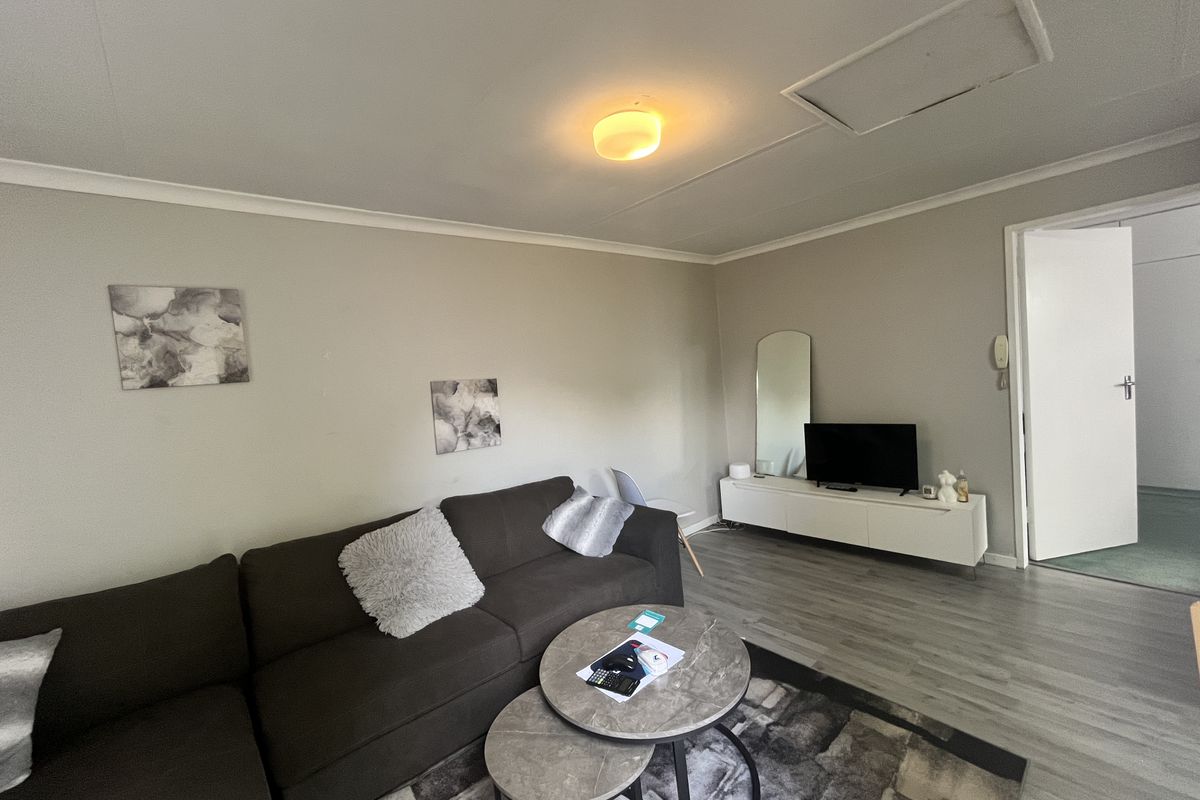 A comfortable living room featuring light-toned laminate flooring, neutral wall finishes, and a ceiling-mounted light fixture.