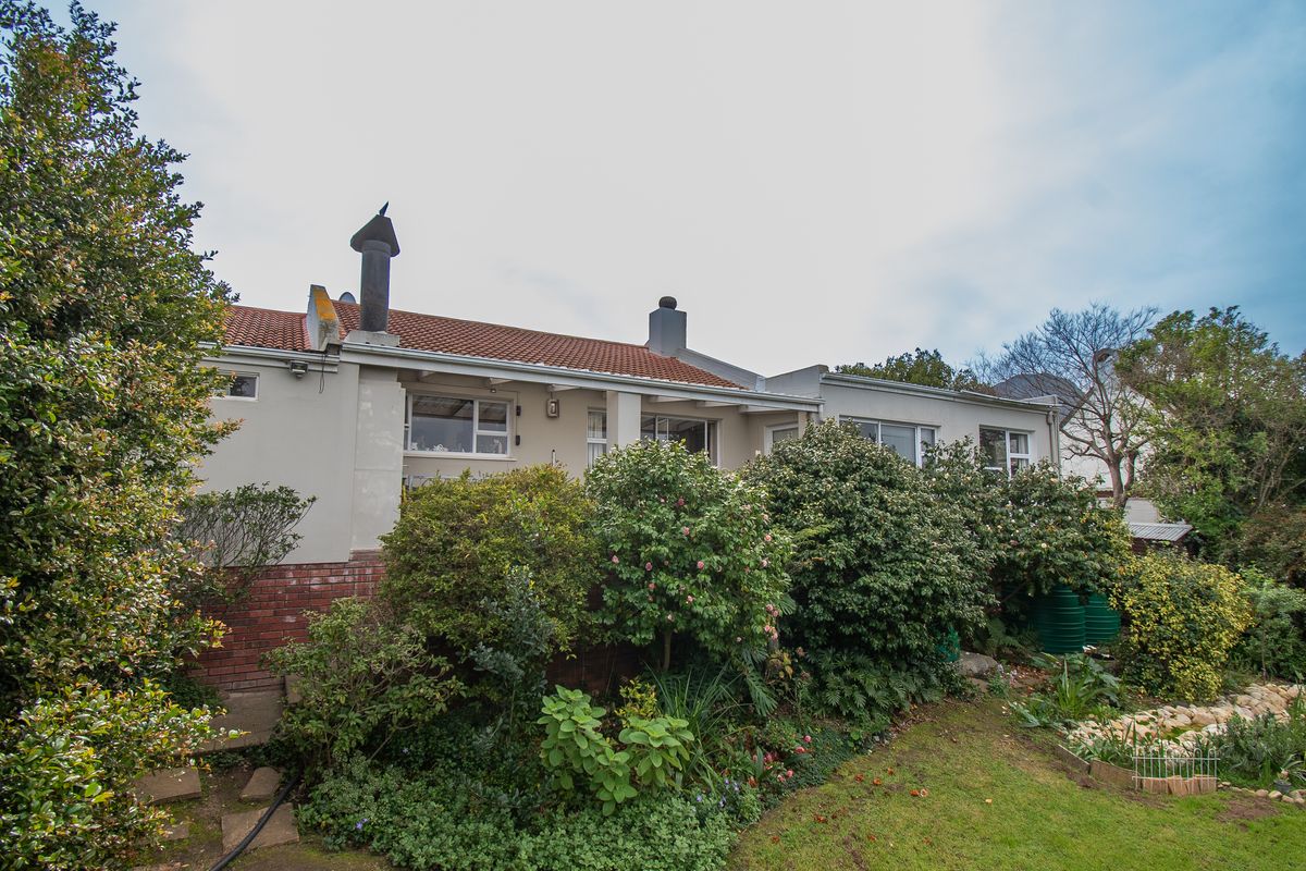 Rear view of the house featuring a terracotta tiled roof, chimneys, and established garden landscaping with integrated rainwater tanks.