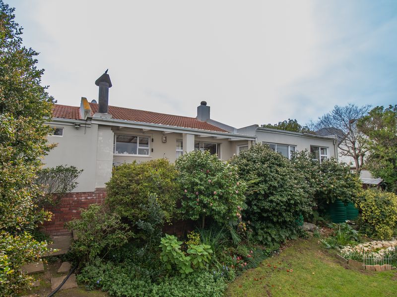 Rear view of the house featuring a terracotta tiled roof, chimneys, and established garden landscaping with integrated rainwater tanks.
