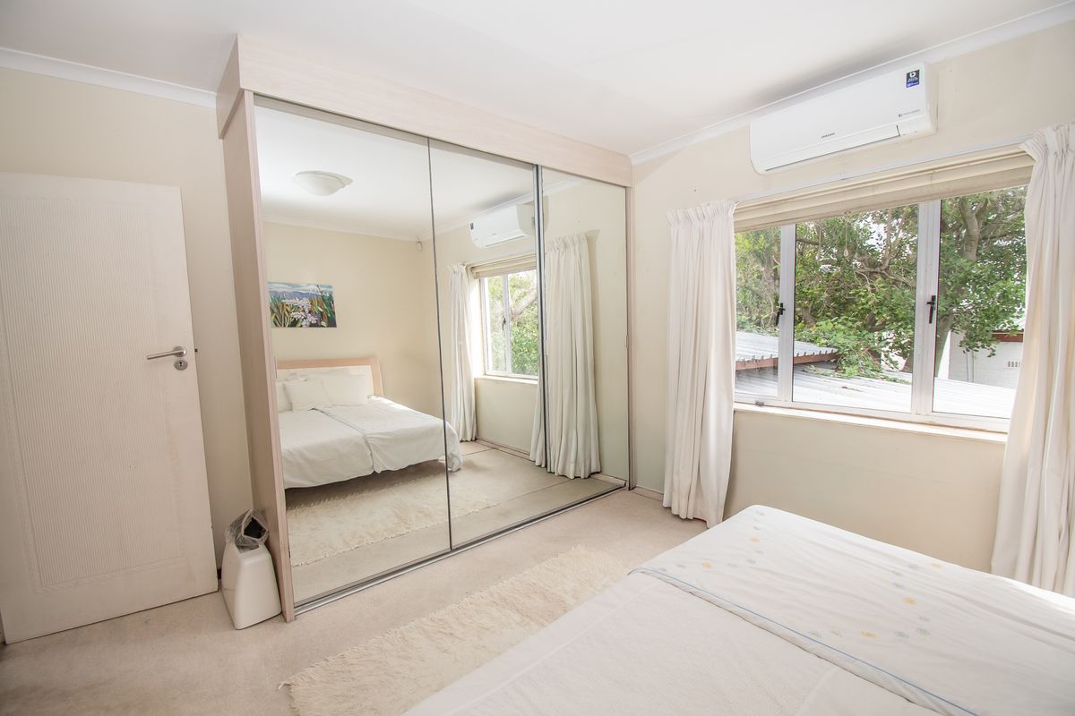 A well-maintained bedroom featuring a large built-in mirrored wardrobe, split-system air conditioning, and aluminium-framed windows overlooking greenery.