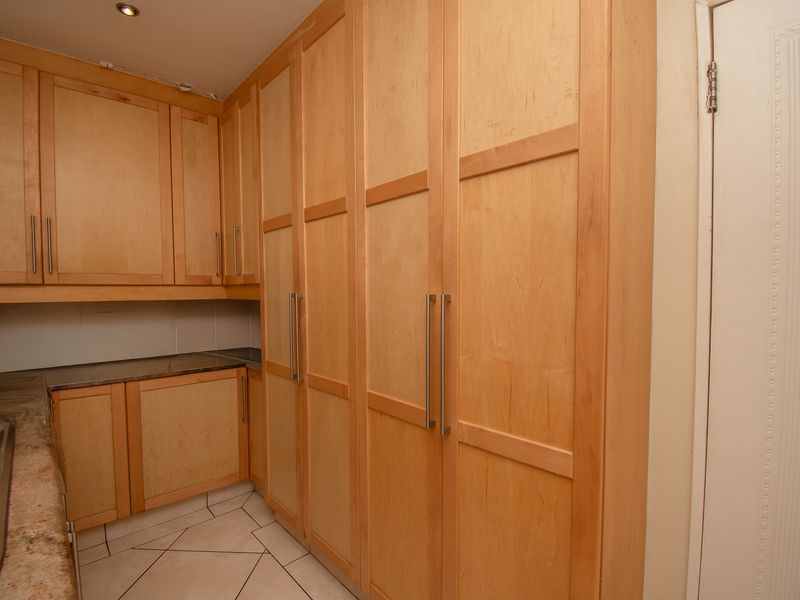 A functional scullery featuring extensive light wood cabinetry, stone countertops, a stainless steel sink, and tiled flooring.