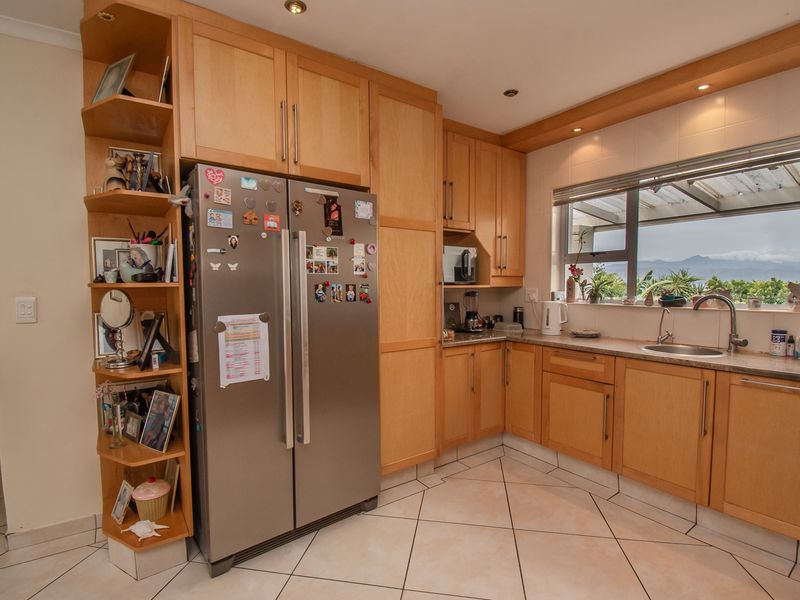 A functional kitchen featuring light wood cabinetry, stone countertops, tiled flooring, and a window with natural light and scenic views.