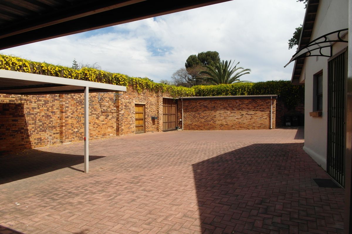 A spacious paved rear courtyard featuring a carport, secure brick boundary walls with climbing plants, and access to a garage and side entrance.