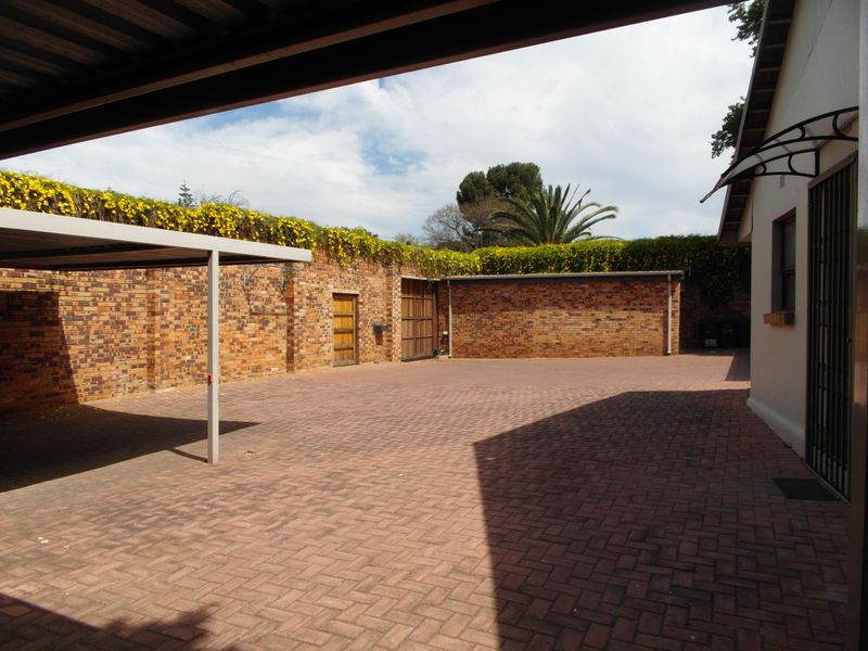 A spacious paved rear courtyard featuring a carport, secure brick boundary walls with climbing plants, and access to a garage and side entrance.