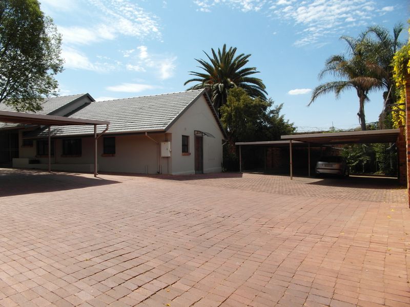 Exterior view of the apartment complex featuring a large paved driveway and covered carport parking areas.