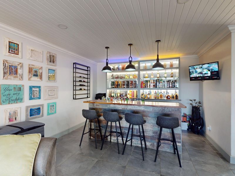 A well-appointed home bar featuring a built-in counter, illuminated shelving, pendant lighting, and tiled flooring, creating an inviting space for entertainment.