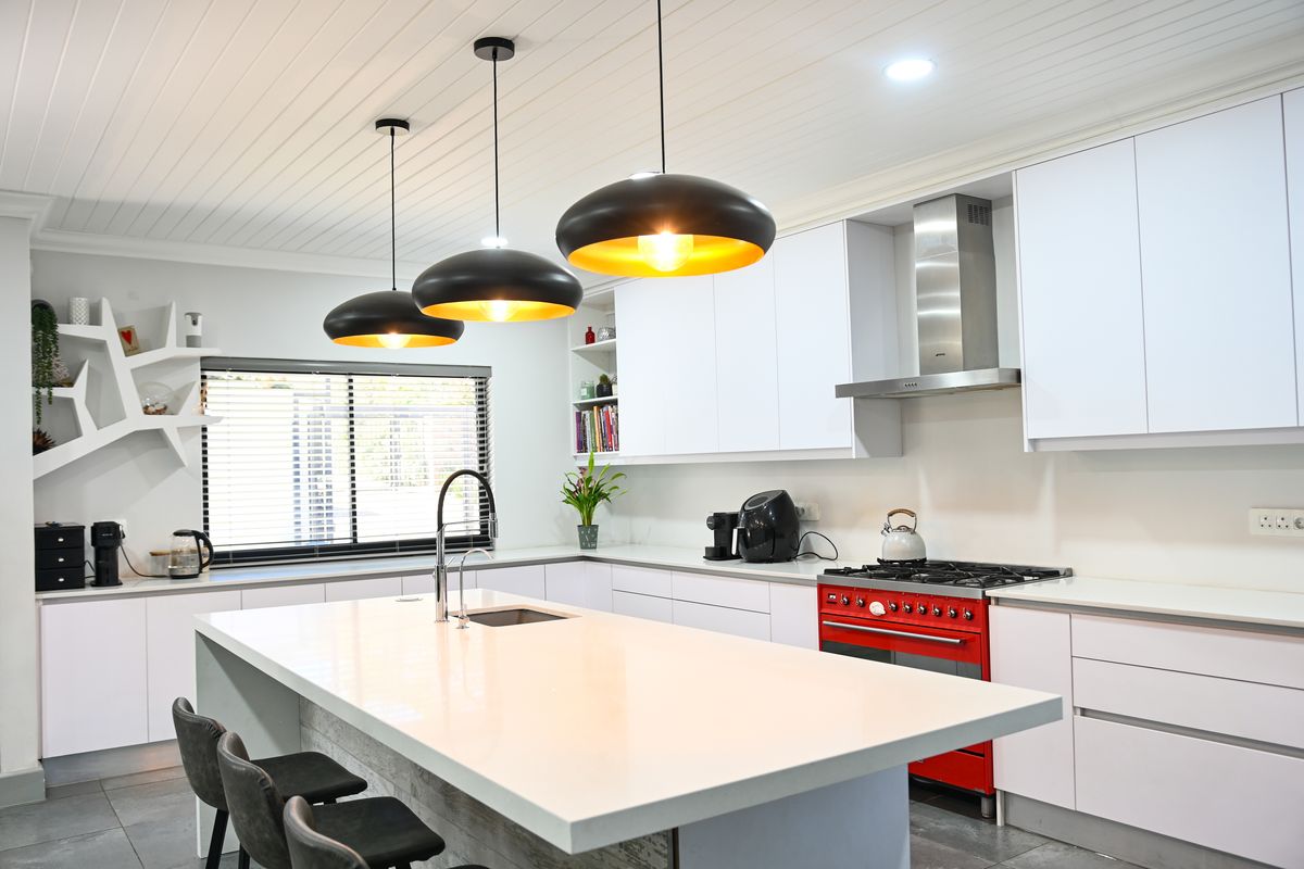 Modern kitchen featuring a large central island with quartz countertops, high-end gas range, stainless steel extractor, and sleek white cabinetry with contemporary pendant lighting.