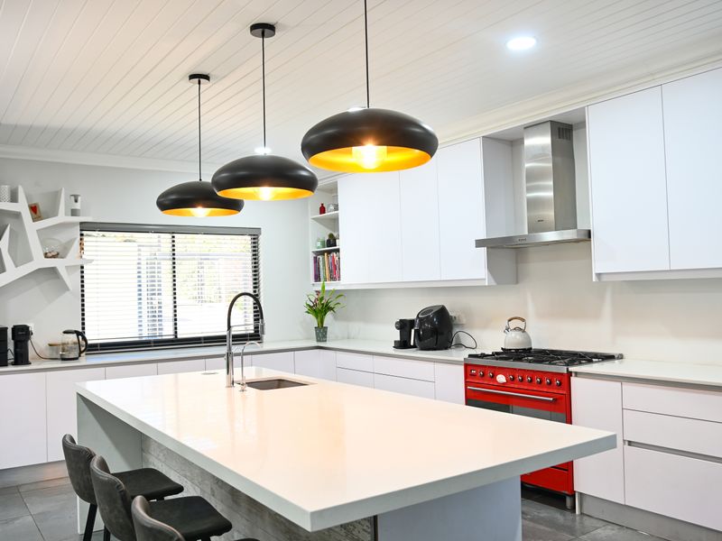 Modern kitchen featuring a large central island with quartz countertops, high-end gas range, stainless steel extractor, and sleek white cabinetry with contemporary pendant lighting.