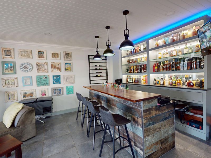 A well-appointed home bar featuring a custom built-in counter, extensive backlit shelving for display, and stylish pendant lighting.