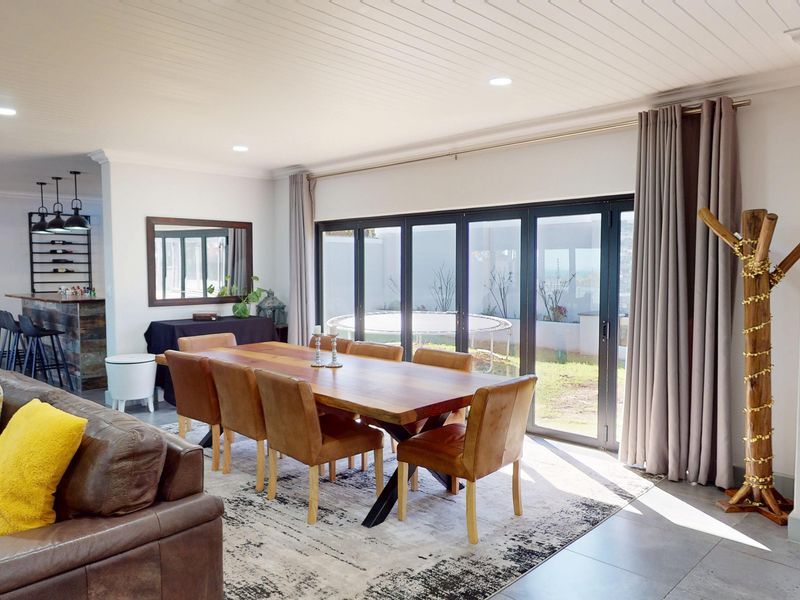 Spacious open-plan living and dining area featuring tiled floors, recessed lighting, and large aluminium stacker doors providing seamless access to the outdoor patio.