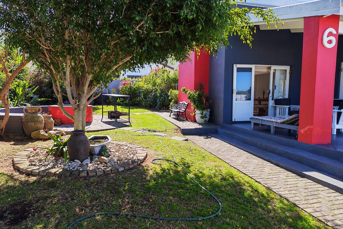 A well-maintained rear garden featuring a paved patio area, a covered veranda, and established landscaping with a brick pathway.
