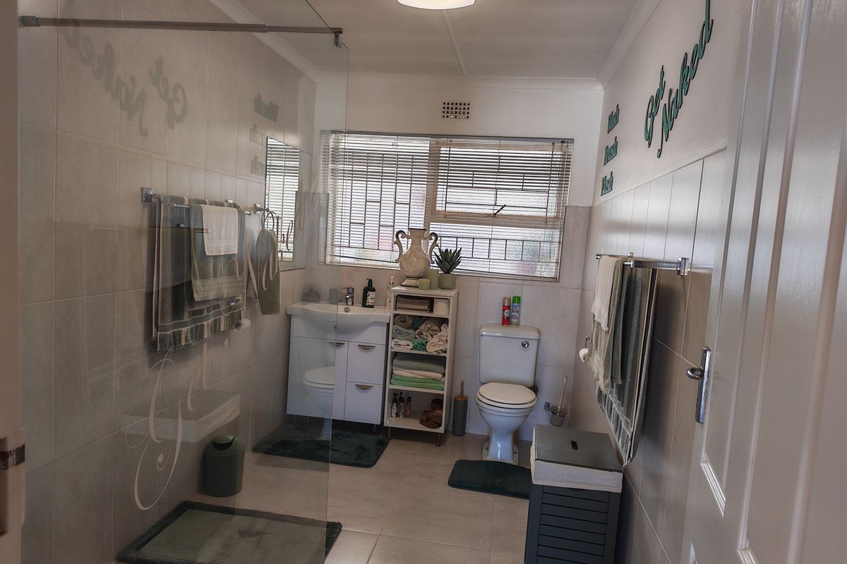 A functional bathroom featuring a glass-enclosed shower, vanity basin, toilet, and neutral wall and floor tiling.