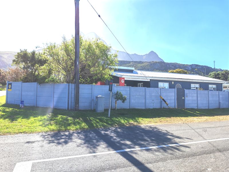 Street-level view of the property featuring a precast concrete boundary wall, pedestrian gate, and mountain backdrop.