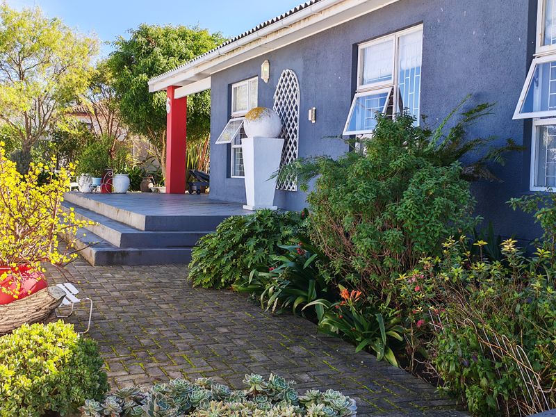 Front elevation of a house featuring a paved walkway, concrete steps leading to a covered porch, and established garden landscaping.