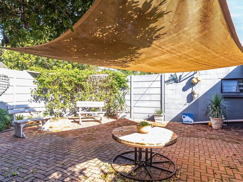 A paved outdoor patio area featuring a shade sail and enclosed by boundary walls, providing a private space for outdoor relaxation.