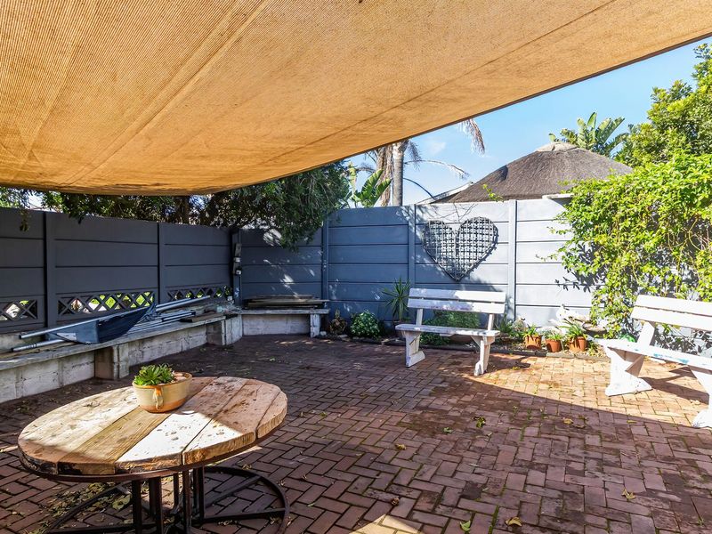 Outdoor patio area featuring brick paving, a large overhead shade sail, and built-in concrete bench seating against a private boundary wall.