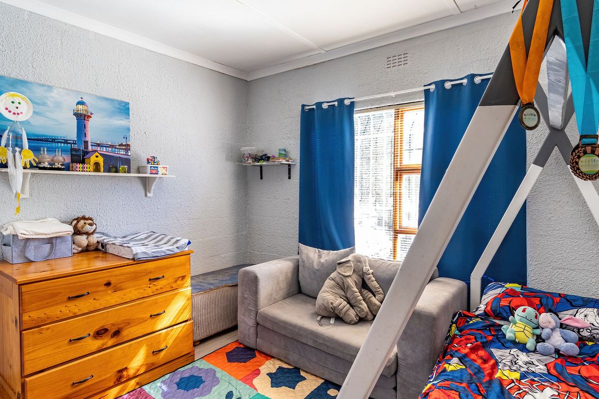 A functional bedroom featuring textured walls, a window with blue curtains, and built-in shelving, providing a comfortable space for rest or play.