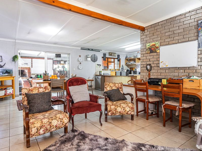 Spacious open-plan living and kitchen area featuring an exposed brick wall, timber ceiling beam, and tiled flooring with direct access to the patio.