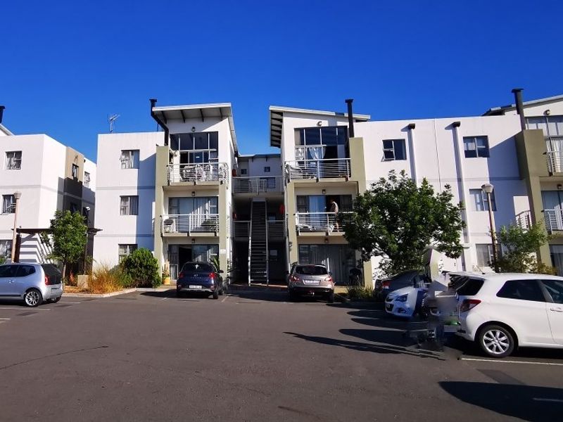 Front elevation of a modern multi-story apartment complex featuring private balconies, metal railings, and an open-air central staircase with dedicated parking.