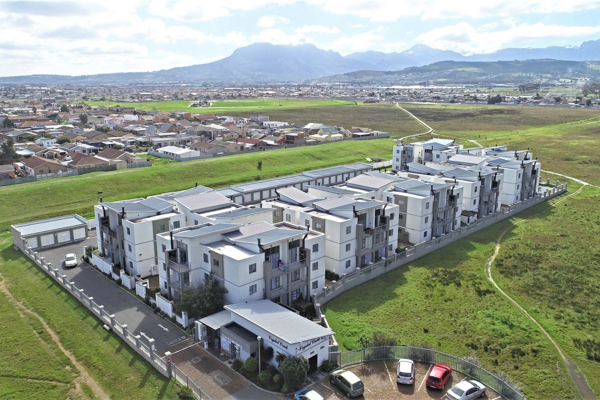 Aerial view of a modern apartment complex featuring multiple residential blocks, paved access roads, and perimeter security fencing in a suburban setting.