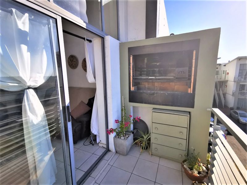 A private balcony featuring a built-in braai, tiled flooring, and sliding glass door access to the interior living space.