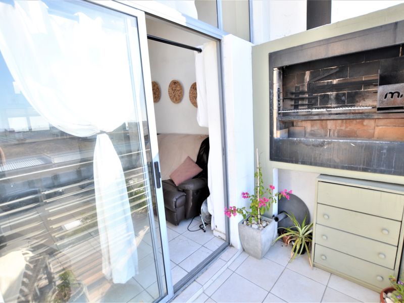 A compact balcony featuring a built-in braai, tiled flooring, and sliding glass door access to the interior living space.
