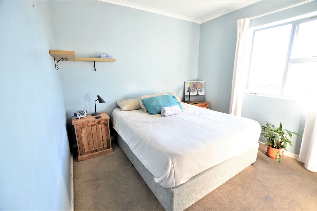 A standard bedroom featuring carpeted flooring, light blue walls, and a window allowing natural light into the space.