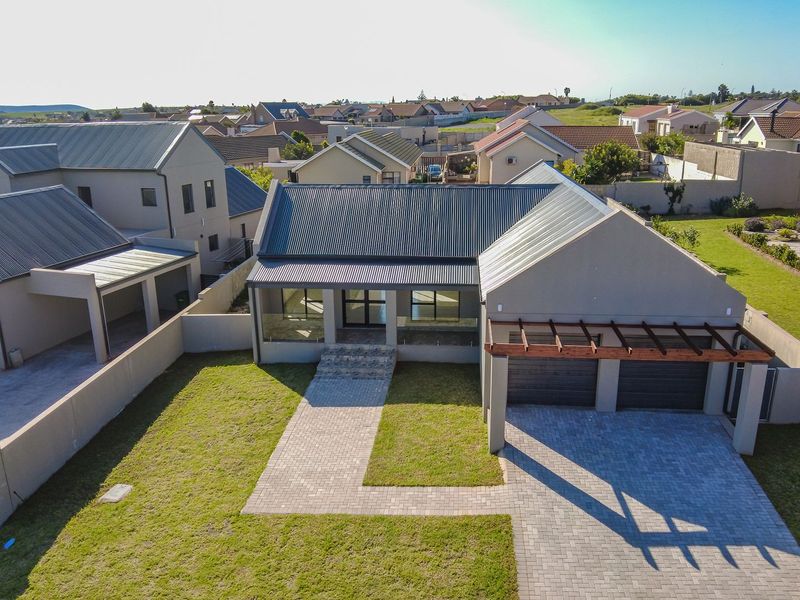 Aerial view of a modern residential property featuring a corrugated metal roof, double garage, paved driveway, and a timber pergola over the entrance.
