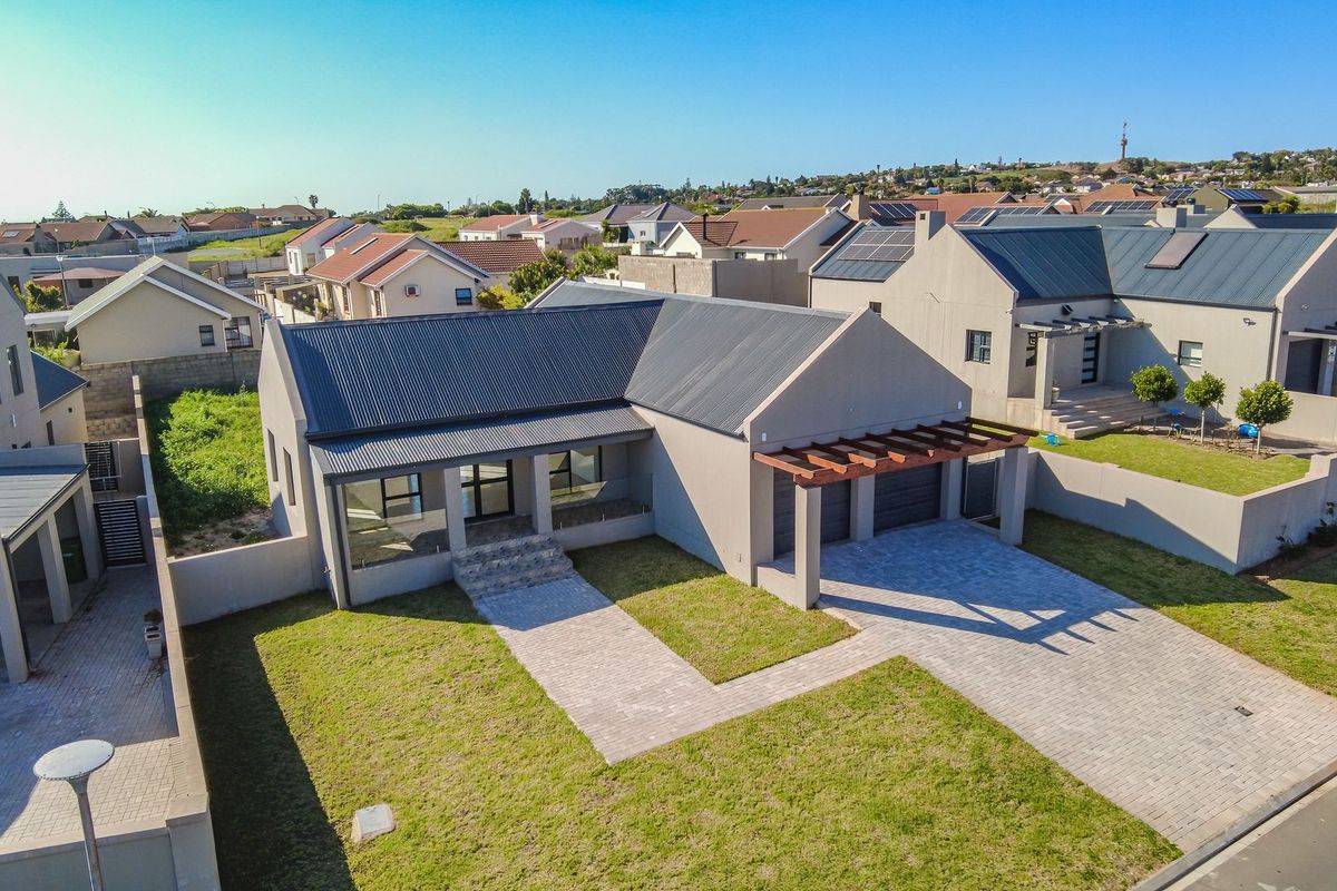 Aerial view of a modern single-story house featuring a corrugated metal roof, paved driveway, double garage, and timber pergola in a residential estate.