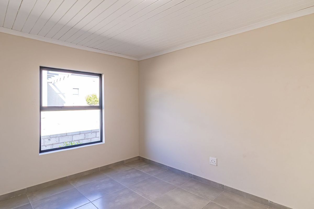 A clean, empty bedroom featuring neutral wall tones, tiled flooring, and a white tongue and groove ceiling with an aluminium window.