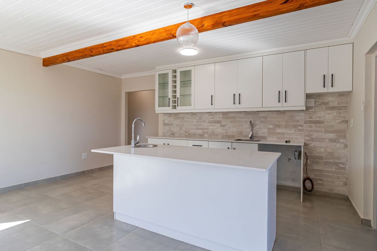 Modern kitchen featuring white cabinetry, stone countertops, a central island, and an exposed timber ceiling beam, awaiting final appliance installation.