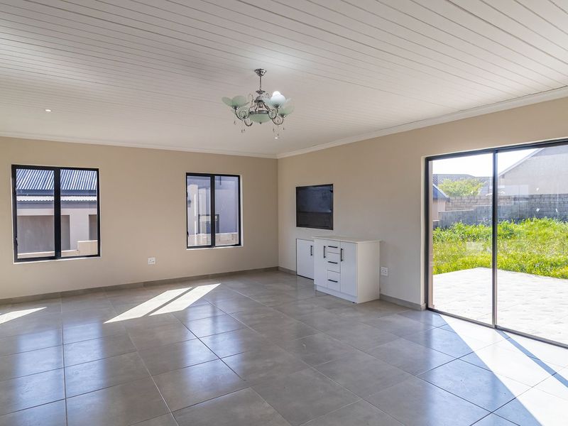 A bright, open-plan living area featuring large sliding glass doors, tiled flooring, and a modern tongue and groove ceiling.