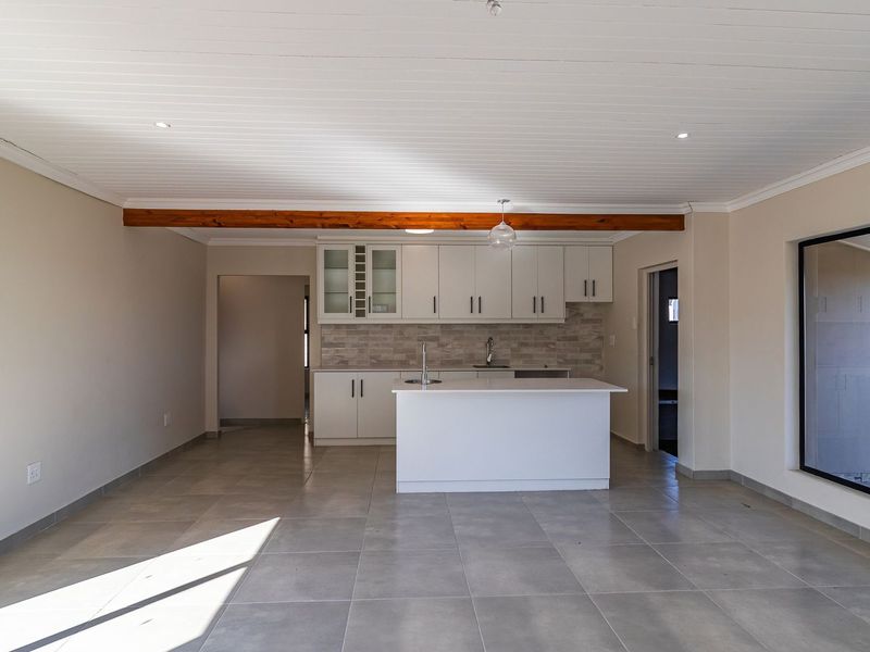 Spacious open-plan kitchen and living area featuring modern white cabinetry, a central island, tiled flooring, and a decorative timber ceiling beam.