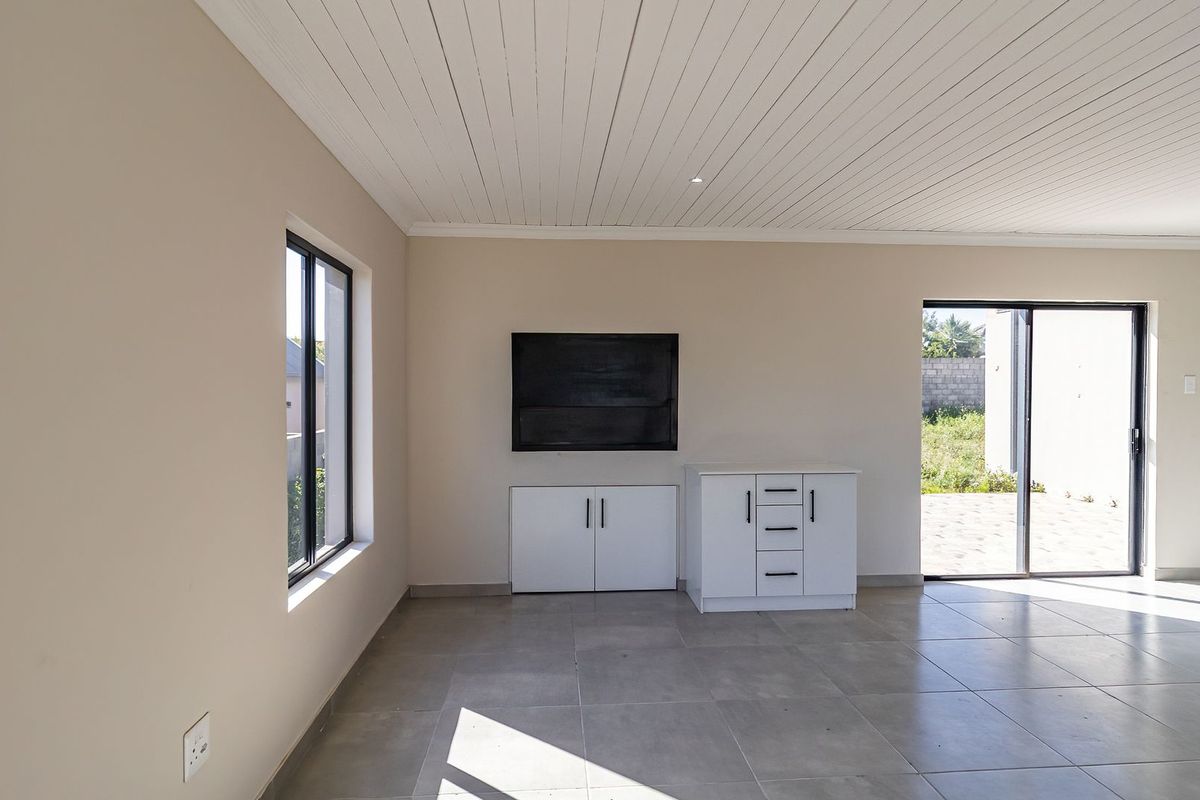 A bright, open-plan living area featuring neutral tiled floors, a white tongue and groove ceiling, and built-in storage cabinetry with direct access to the outdoors.