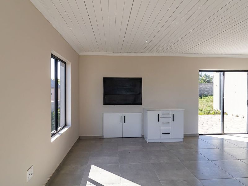 A bright, open-plan living area featuring neutral tiled floors, a white tongue and groove ceiling, and built-in storage cabinetry with direct access to the outdoors.