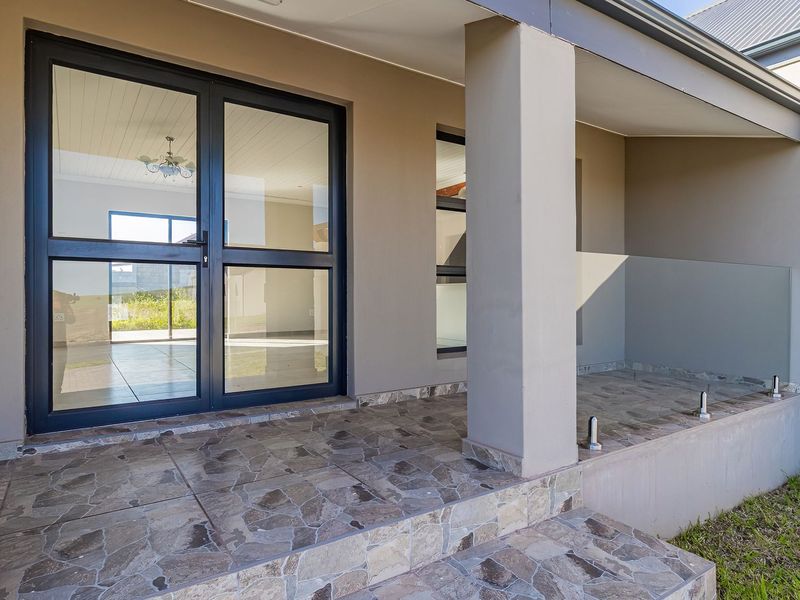 A covered patio area featuring stone-clad flooring, a modern glass balustrade, and aluminium-framed glass doors leading into the home.