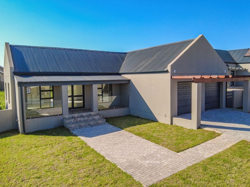 Modern single-story house featuring a corrugated metal roof, double garage, paved driveway, and a welcoming entrance with stone steps and a timber pergola.