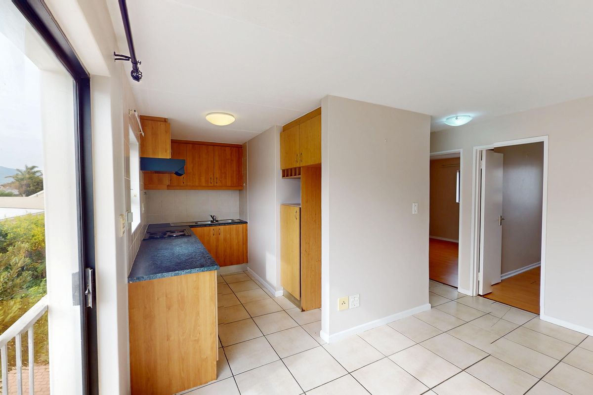 A functional kitchen featuring wooden cabinetry, laminate countertops, a built-in hob, and tiled flooring, with direct access to an outdoor balcony area.